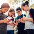 Four adolescents standing in a group, looking on their smart phones.